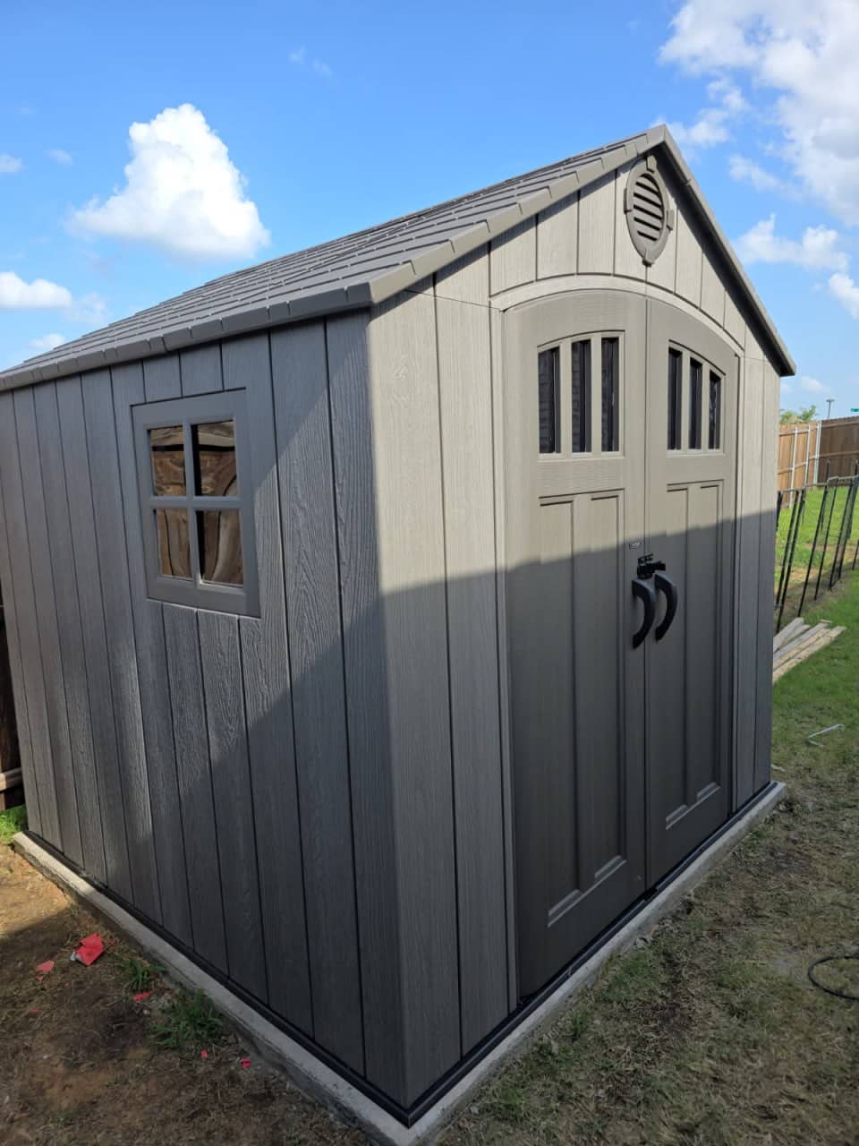 Two-tone wooden storage shed with arched double doors installed in a backyard