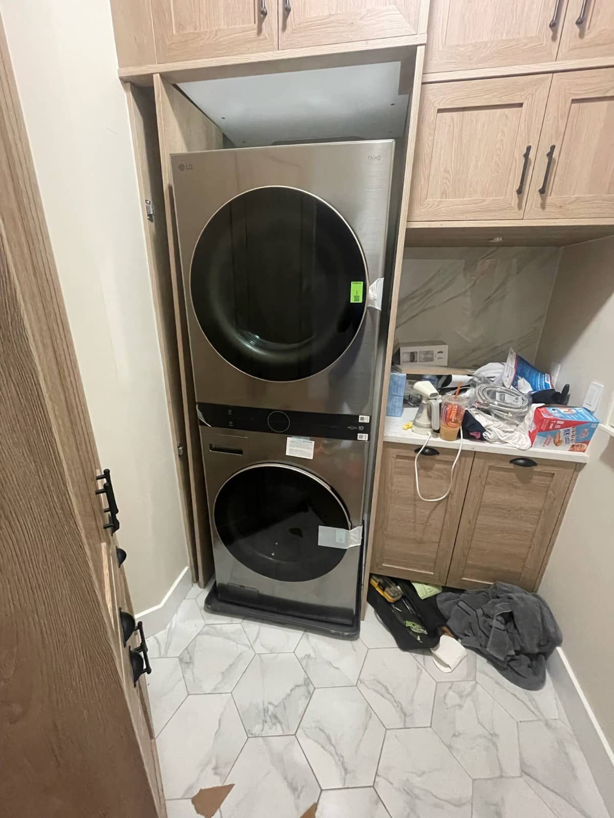 LG stacked washer and dryer unit installed in a laundry room with oak cabinetry